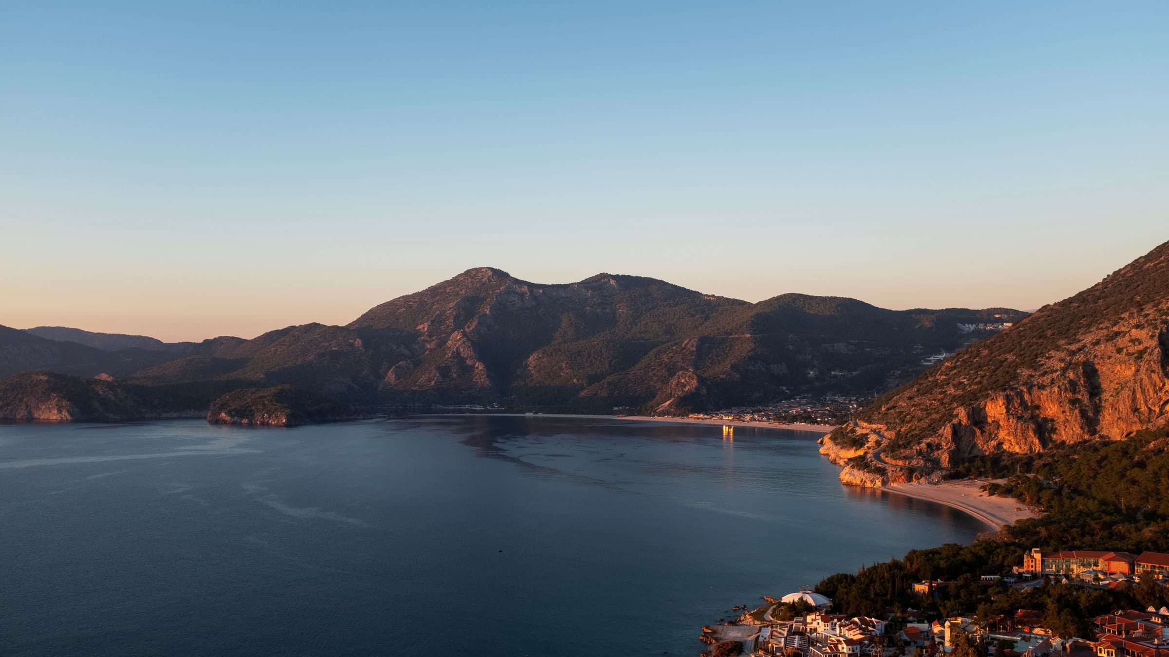 The coastline near Fethiye at dawn — headlands receding into haze, the lagoon spit and the town catching the first low light.