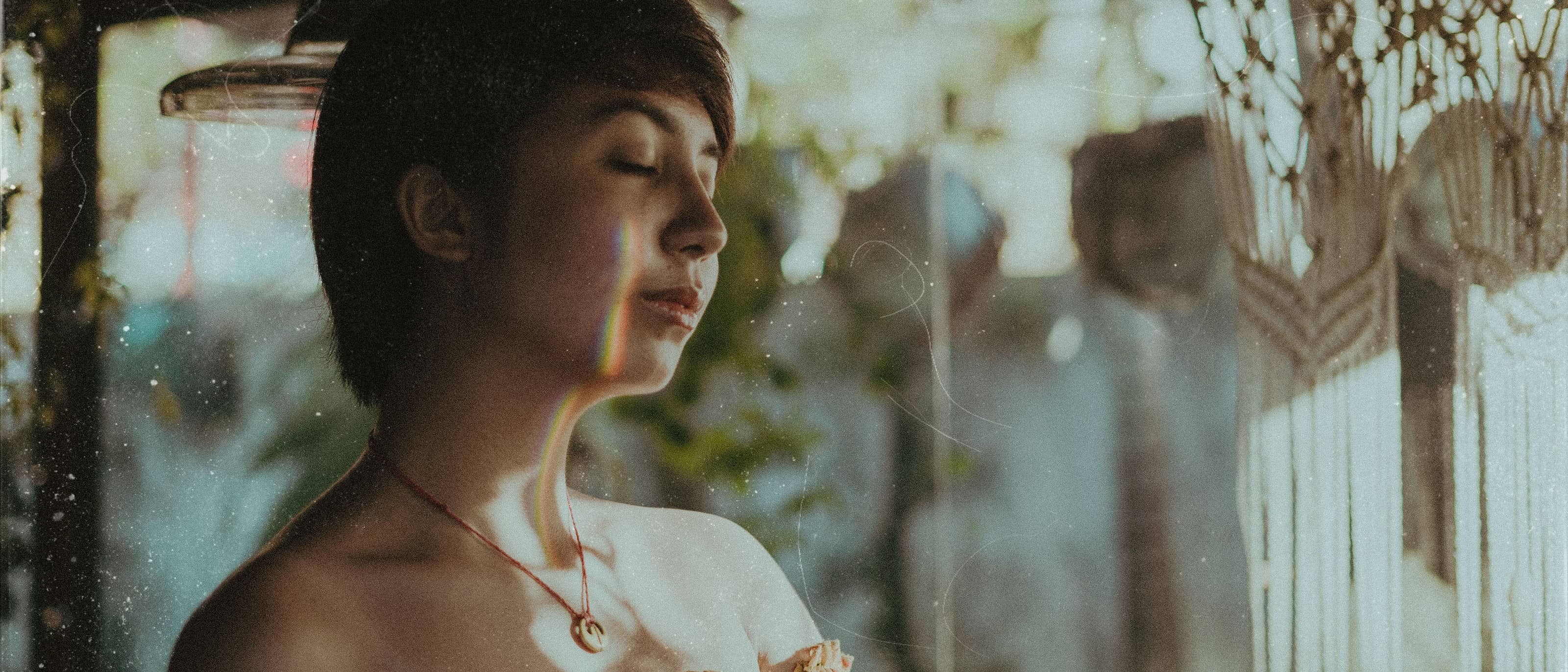 A woman with her eyes closed in hazy window light, warm honey tones across her face and shoulders.