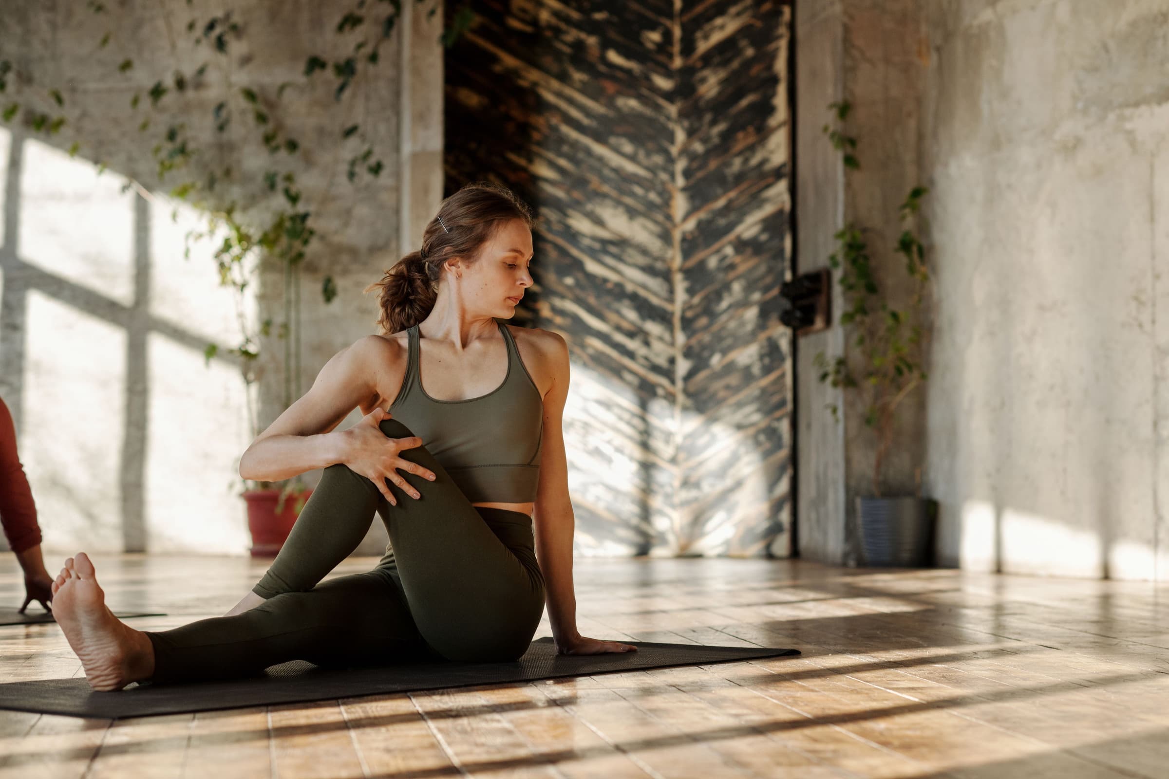 A person seated on a mat in a warm, plain room, turning into a slow spinal twist.