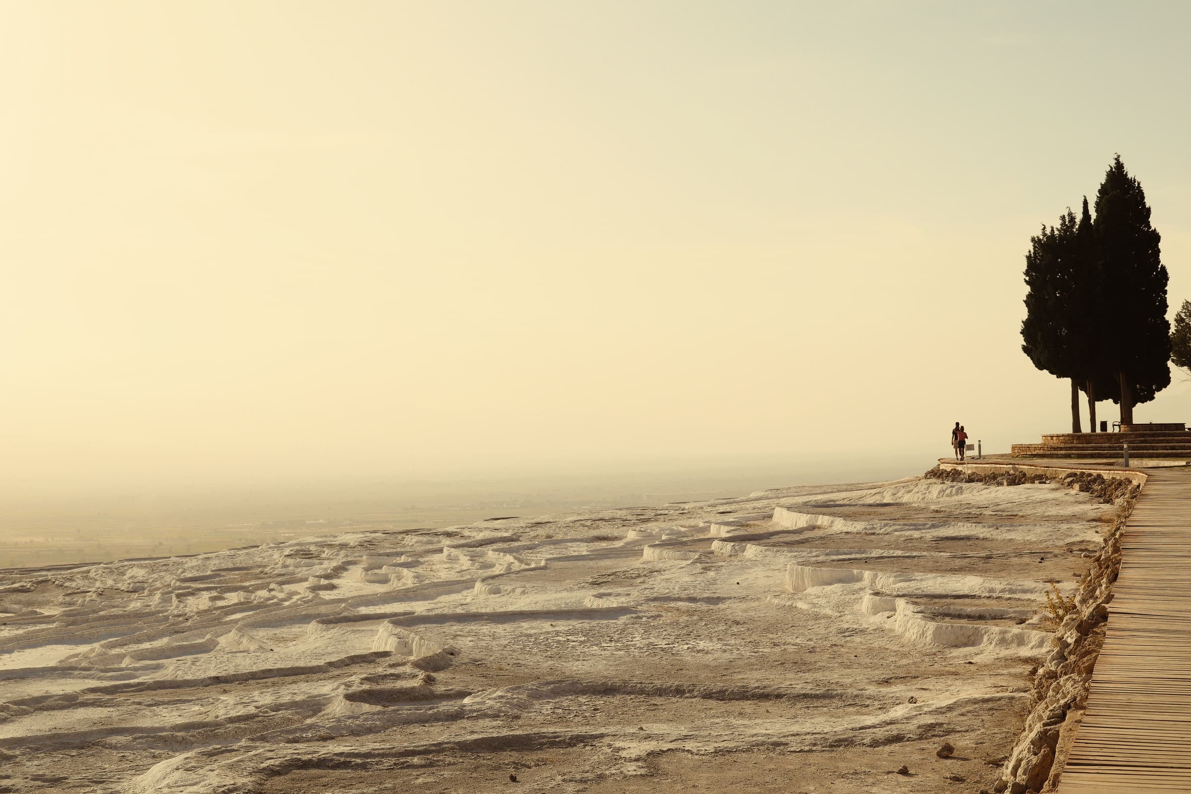 The white travertine shelves of Pamukkale at golden hour, cypresses on the ridge and a single figure at the edge.