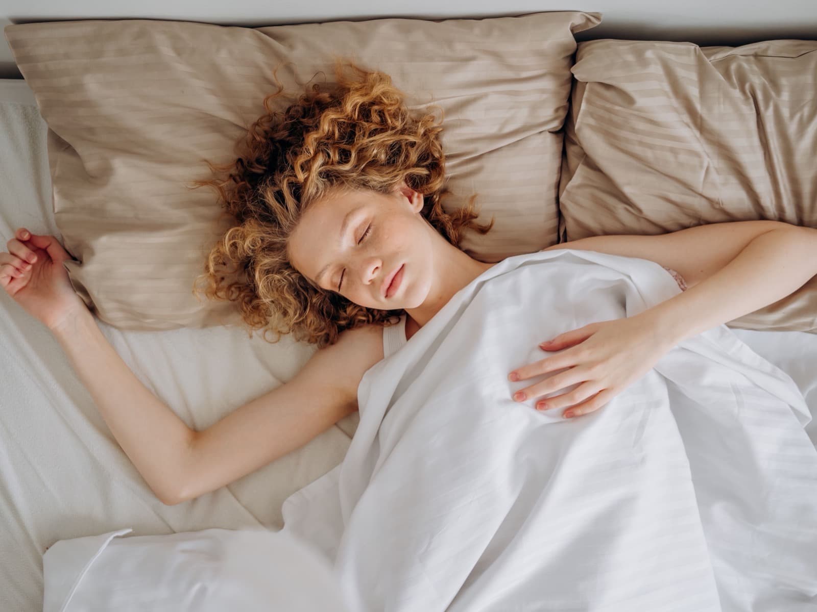 A woman asleep on her back in white linen, seen from above in soft daylight.